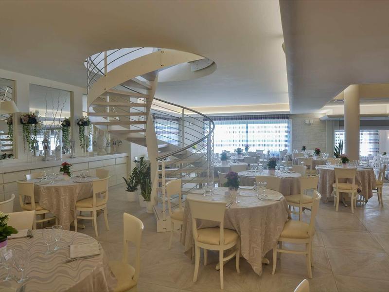 Restaurant d'hôtel élégant avec tables rondes et escalier en colimaçon moderne dans un cadre lumineux.