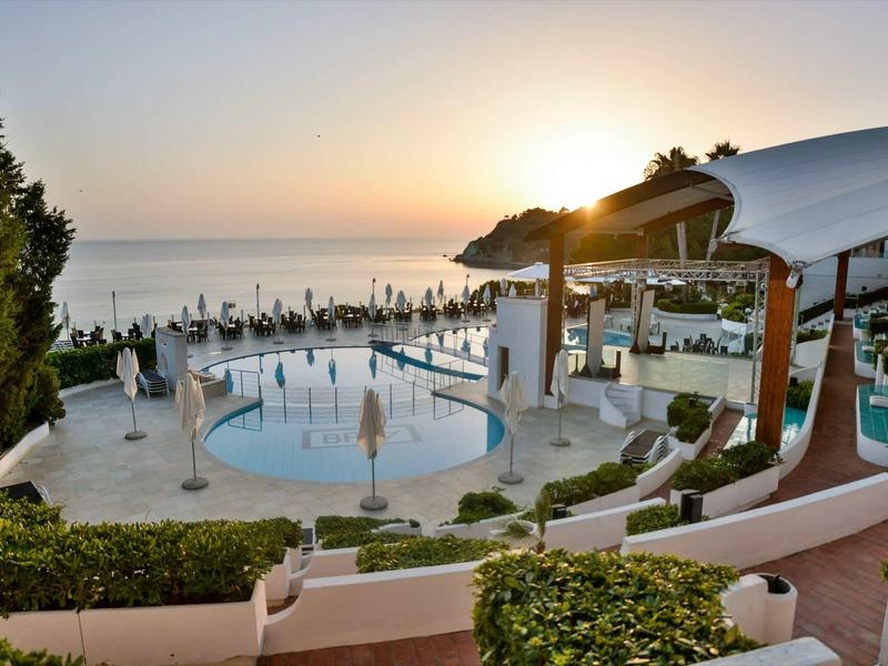 Espace piscine avec parasols et vue sur la mer au coucher du soleil.