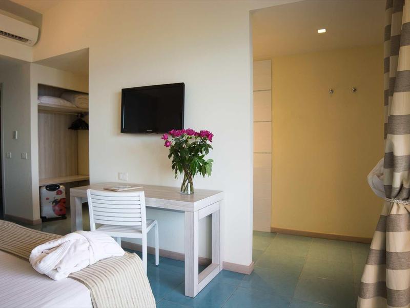 Chambre d'hôtel lumineuse avec bureau, chaise, télévision et bouquet de fleurs.