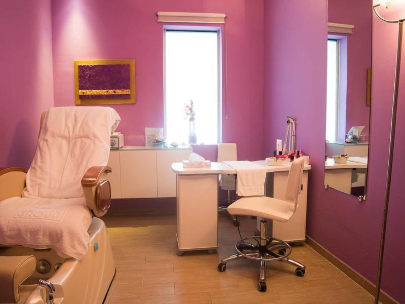 Salon de manucure moderne avec murs roses, fauteuils confortables et espace de travail bien éclairé.