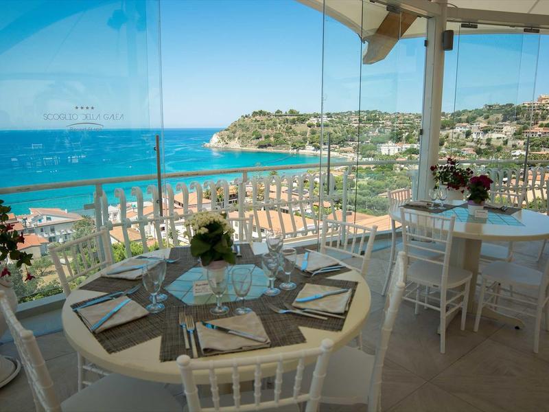 Terrasse avec tables dressées donnant sur la mer bleue et les collines.