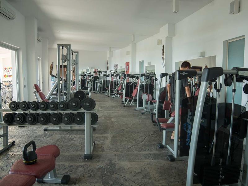 Salle de sport moderne avec divers appareils d'entraînement et haltères dans une pièce lumineuse et spacieuse.