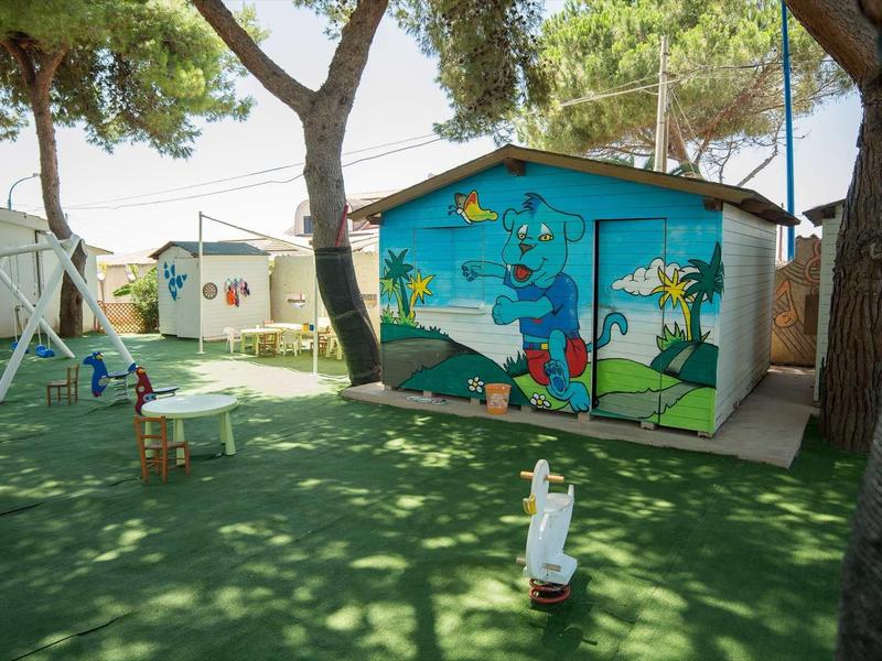 Aire de jeux colorée pour enfants avec des cabanes peintes et des équipements de jeu à l'ombre.