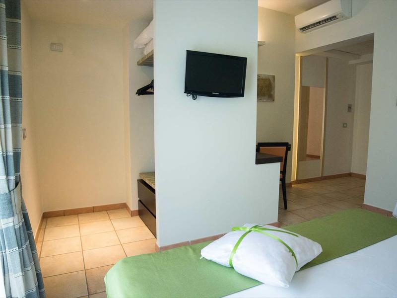 Chambre d'hôtel lumineuse avec lit vert, télévision murale et petit bureau.