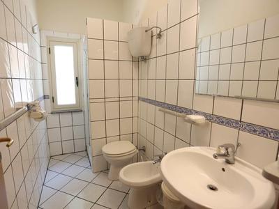Compact bathroom with white tiled walls, sink, toilet, and bidet.