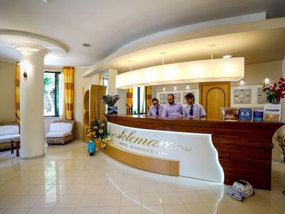 Helle Hotellobby mit geschwungenem Empfangstresen, Personal und Sitzbereichen.