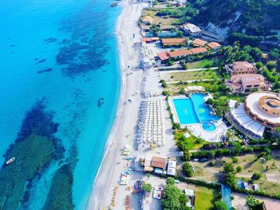 Aerial view of a beach with clear blue water, empty loungers, and few people.