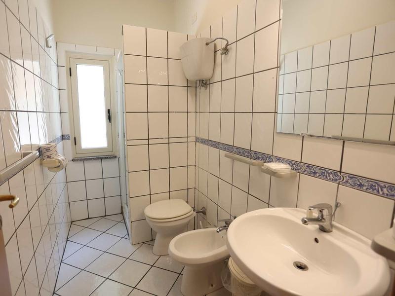 Compact bathroom with white tiled walls, sink, toilet, and bidet.