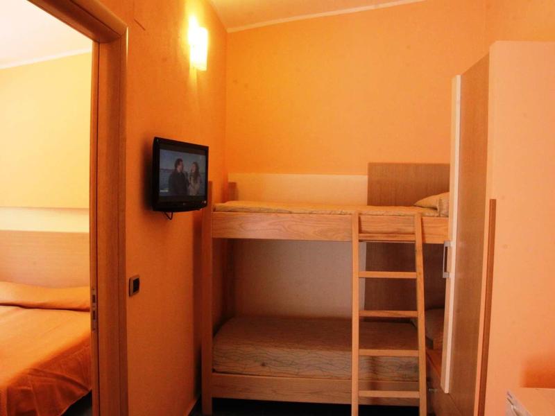 Small room with wooden bunk bed, wall-mounted TV, and adjacent bedroom visible through doorway.