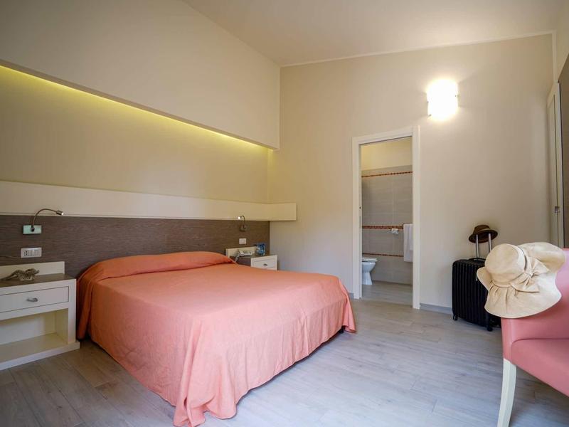 Brightly furnished hotel room with double bed, nightstands, and a view into the bathroom.