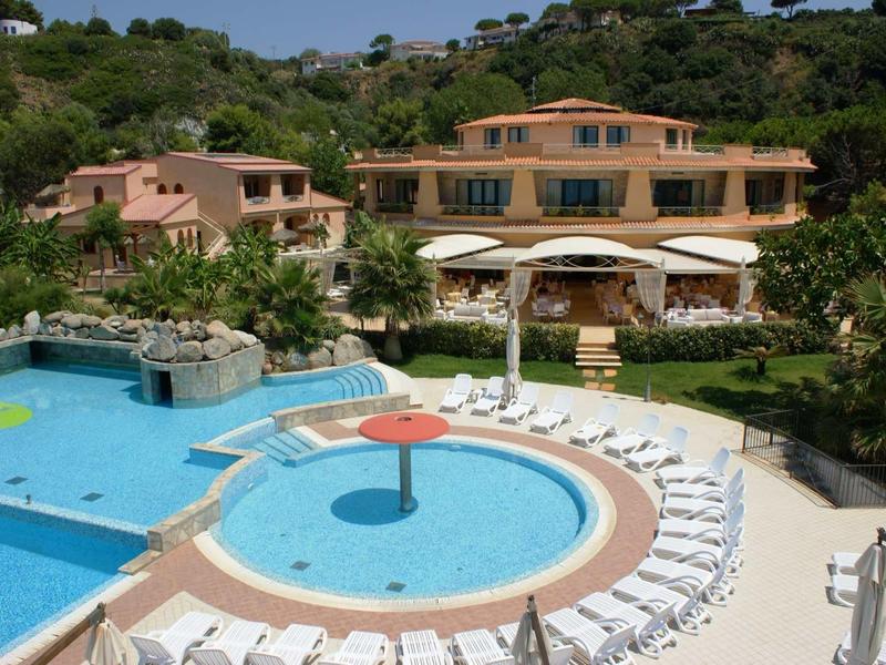 Outdoor pool area with circular kiddie pool, sun loungers, and Mediterranean-style hotel building in background.