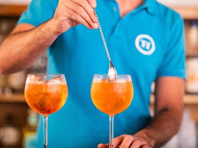 Barman remue deux cocktails orange dans de grands verres à vin.