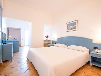 Chambre d'hôtel lumineuse avec lit double, mobilier bleu rembourré et sol en terre cuite.