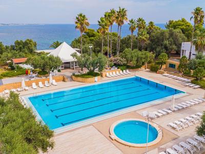 Grande piscine extérieure avec chaises longues et palmiers dans un hôtel en bord de mer.