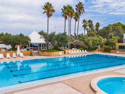 Piscine extérieure avec chaises longues, parasols et palmiers dans un hôtel sous un ciel bleu.