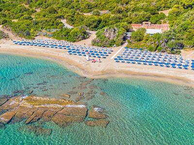 Plage claire avec parasols bleus et eau turquoise près d'une colline boisée