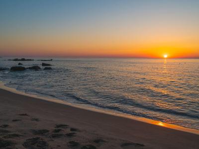 Coucher de soleil sur une mer calme avec une plage de sable au premier plan.