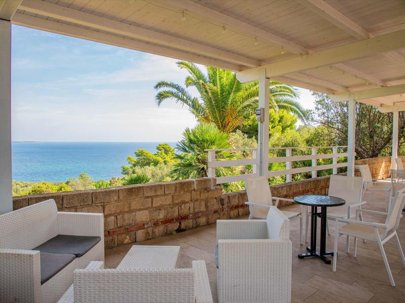 Terrasse couverte avec mobilier blanc donnant sur la mer et des palmiers.