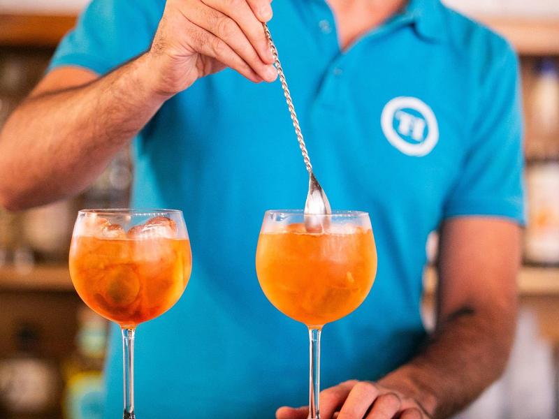 Barman remue deux cocktails orange dans de grands verres à vin.