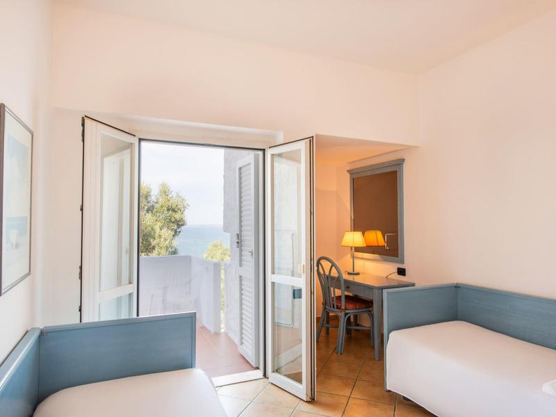 Chambre d'hôtel lumineuse avec lit de jour et porte vitrée ouverte sur balcon.