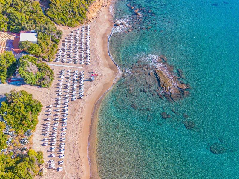 Vue aérienne d'une plage avec chaises longues et eau turquoise claire à côté d'une végétation luxuriante.