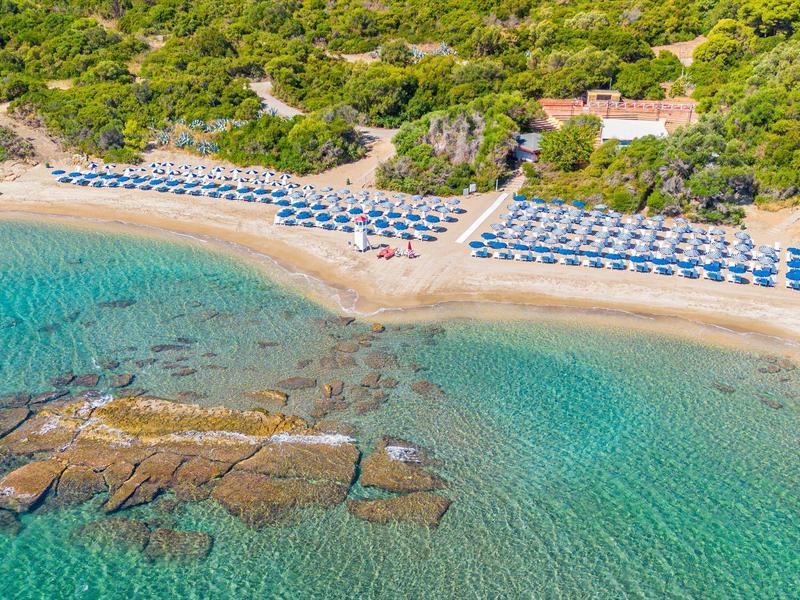 Plage claire avec parasols bleus et eau turquoise près d'une colline boisée