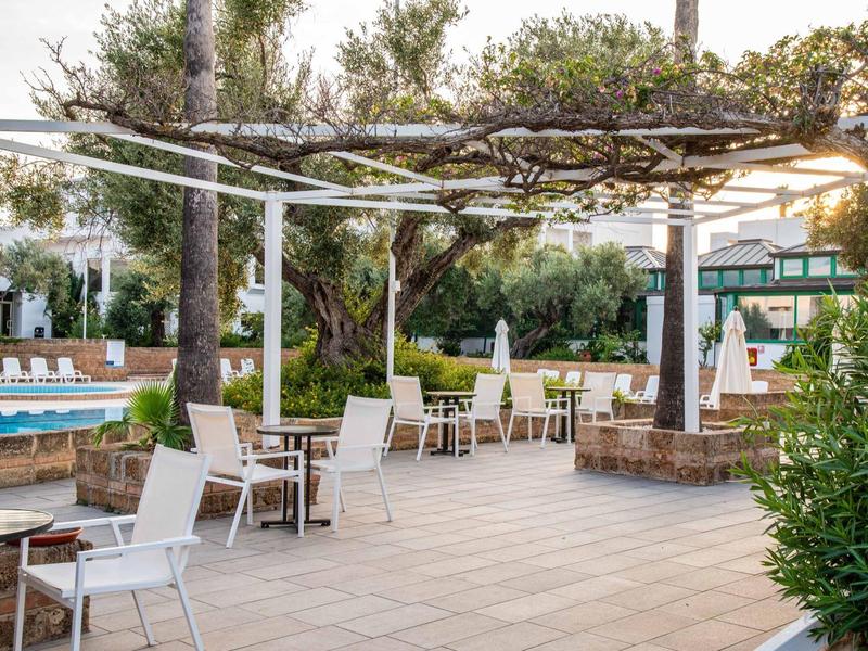 Terrasse d'hôtel avec sièges, parasols et plantes autour d'une piscine.