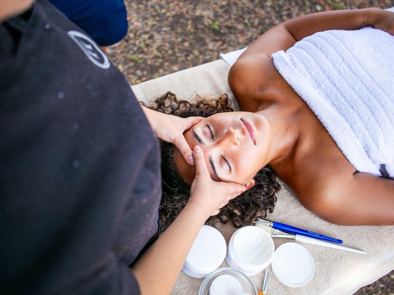 Femme recevant un massage du visage, allongée sur une table de spa avec une serviette.