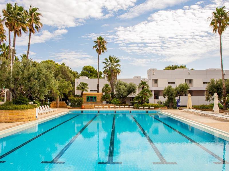 Grand bassin extérieur avec eau bleue et palmiers dans le jardin de l'hôtel.