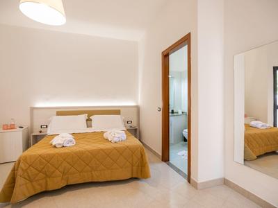 Chambre d'hôtel lumineuse avec lit double, couvre-lit jaune, tables de chevet et grand miroir.