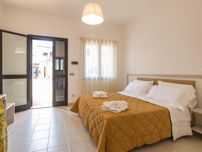 Jasny pokój w hotelu z otwartym wejściem, dwoma łóżkami z brązowymi narzutami i białymi poduszkami.