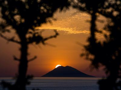 Coucher de soleil derrière une île encadrée par des arbres en silhouette au-dessus de la mer.