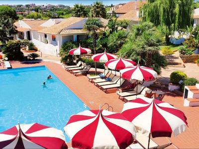 Widok na basen hotelowy z czerwono-białymi parasolami i leżakami.