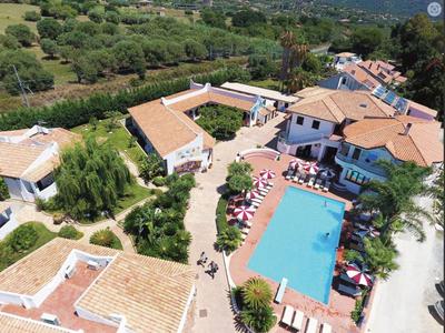 Un complexe hôtelier avec plusieurs bâtiments et une grande piscine bleue entourée de parasols.