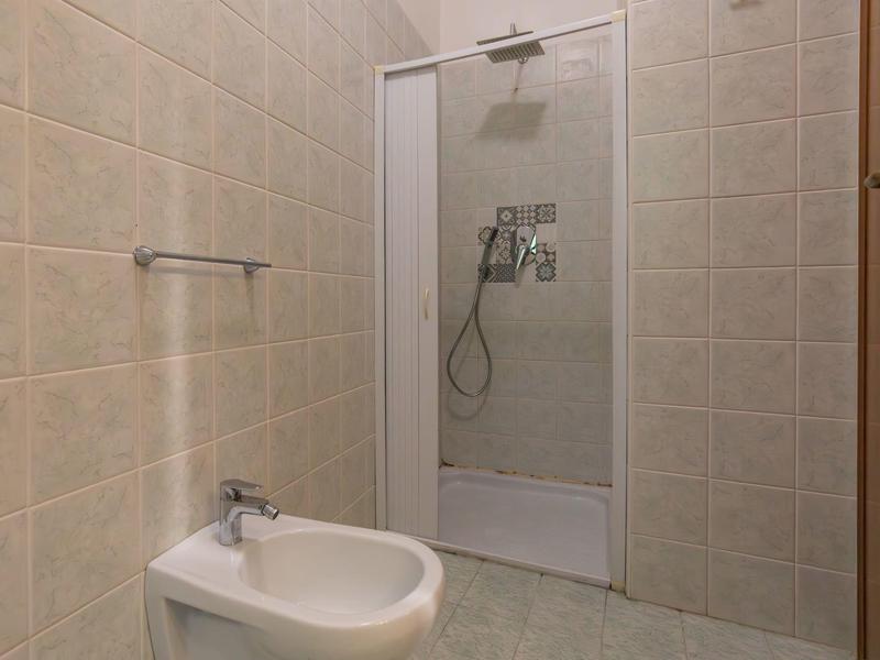 Petite salle de bain avec cabine de douche et bidet, carrelage beige et équipements basiques.