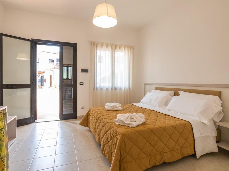 Chambre d'hôtel lumineuse avec entrée ouverte, deux lits avec couvertures dorées et serviettes.