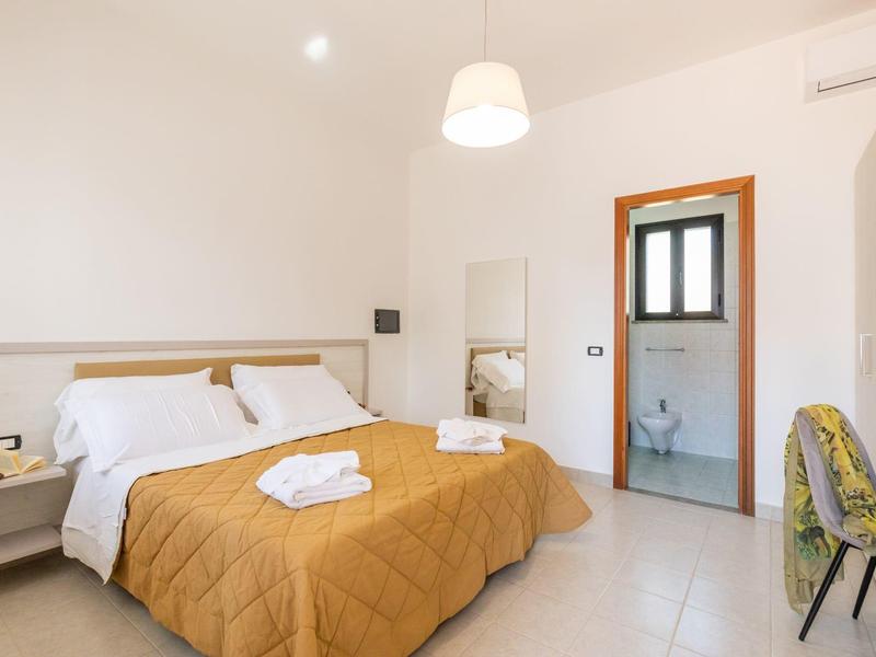 Chambre d'hôtel moderne avec lit double, couvre-lit jaune, chaise et salle de bain attenante.