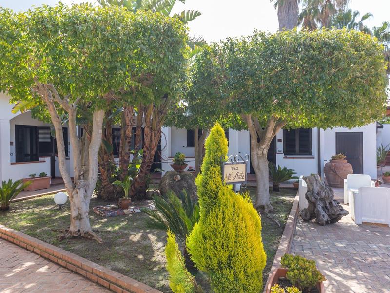 Cour intérieure verte avec arbres et coin salon devant des bâtiments d'hôtel blancs au soleil.