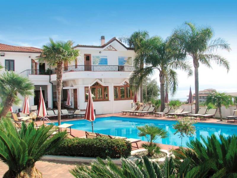 Hôtel avec piscine, palmiers et parasols dans un cadre ensoleillé.