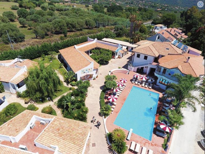Un complexe hôtelier avec plusieurs bâtiments et une grande piscine bleue entourée de parasols.