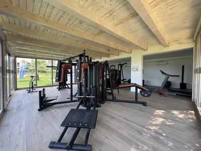 Heller Fitnessraum mit verschiedenen Trainingsgeräten und großem Fenster mit Blick ins Freie.