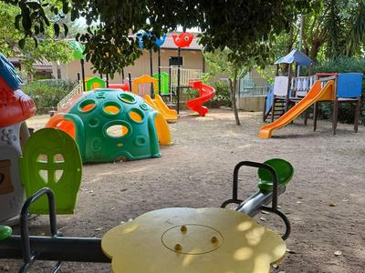 Aire de jeux colorée avec bascules à ressort et structures d'escalade sous des arbres.