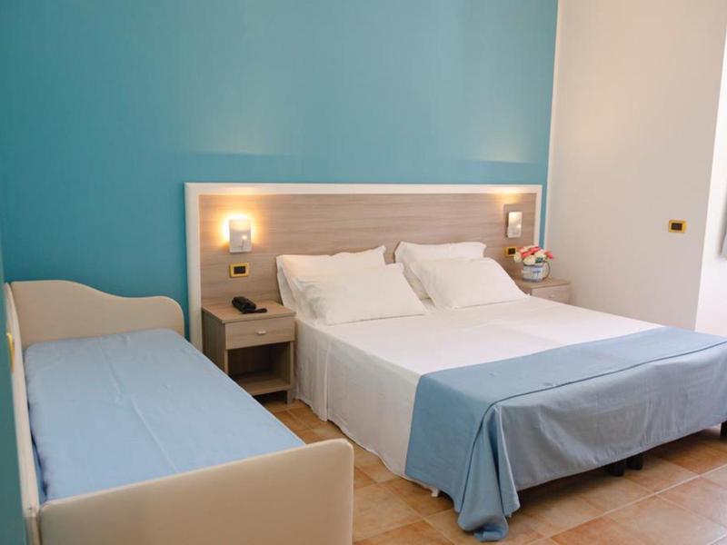 Chambre d'hôtel avec grand lit double et un petit lit simple, murs bleus, ambiance lumineuse.