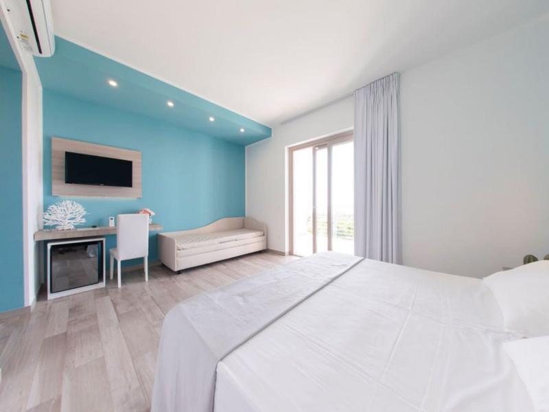 Chambre d'hôtel claire avec lit double, canapé, bureau et porte-fenêtre donnant sur balcon.