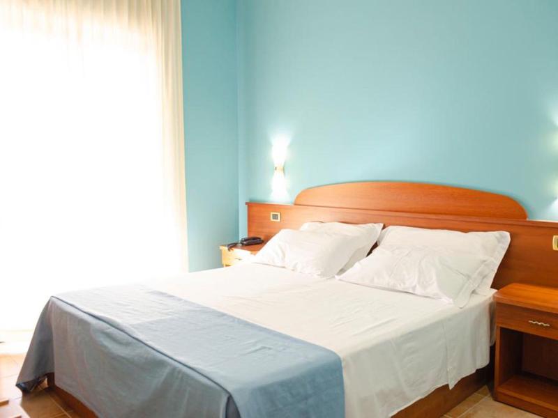 Chambre d'hôtel lumineuse avec lit double, draps blancs et murs bleus.