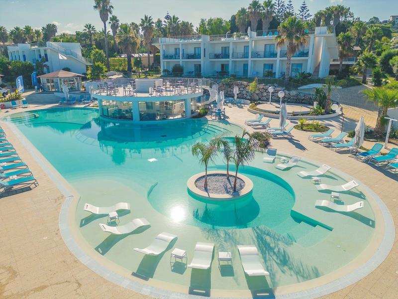 Piscine extérieure avec bar central rond et transats dans un hôtel sous un ciel clair.