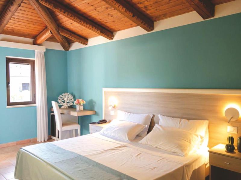 Chambre d'hôtel lumineuse avec mur vert, lit double, bureau et lumière douce.