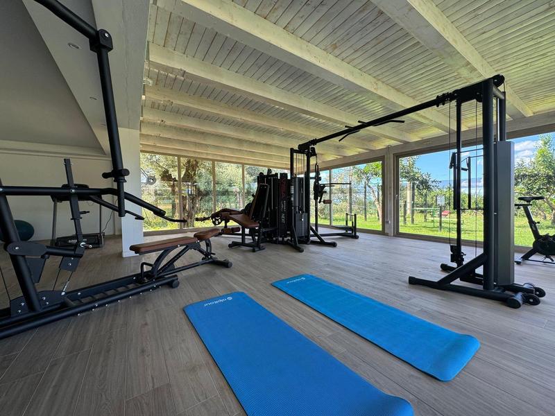 Salle de sport lumineuse avec tapis bleus et équipements modernes, vue sur jardin extérieur.