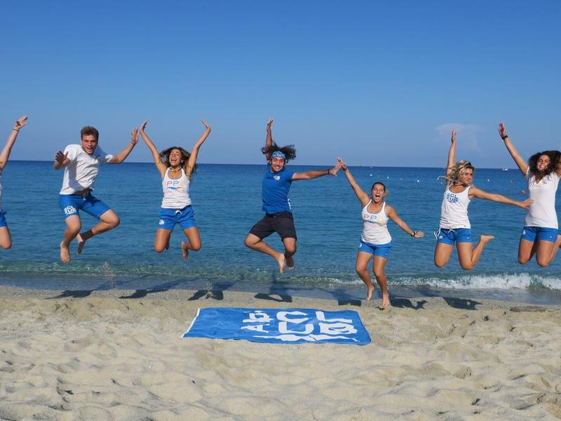 Groupe de personnes sautant joyeusement sur une plage ensoleillée avec une mer bleue en arrière-plan.