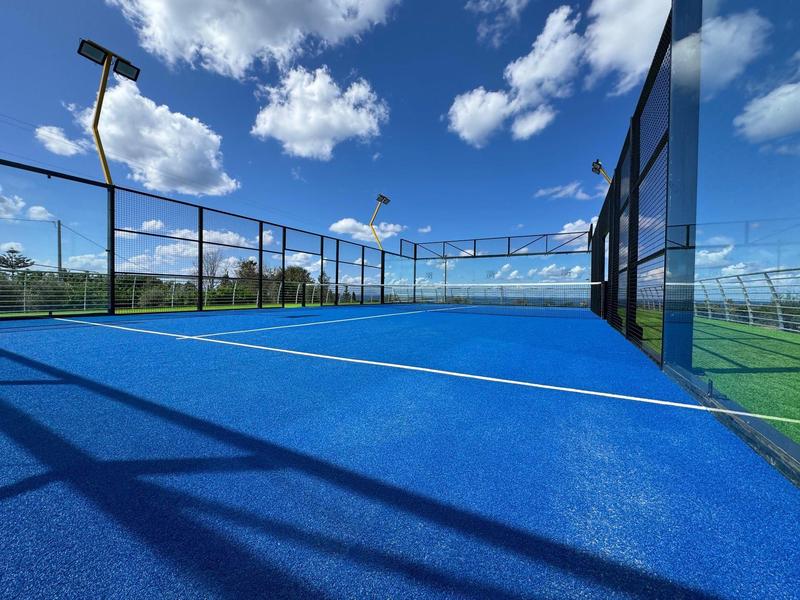 Terrain de padel extérieur avec surface bleue et ciel partiellement nuageux.